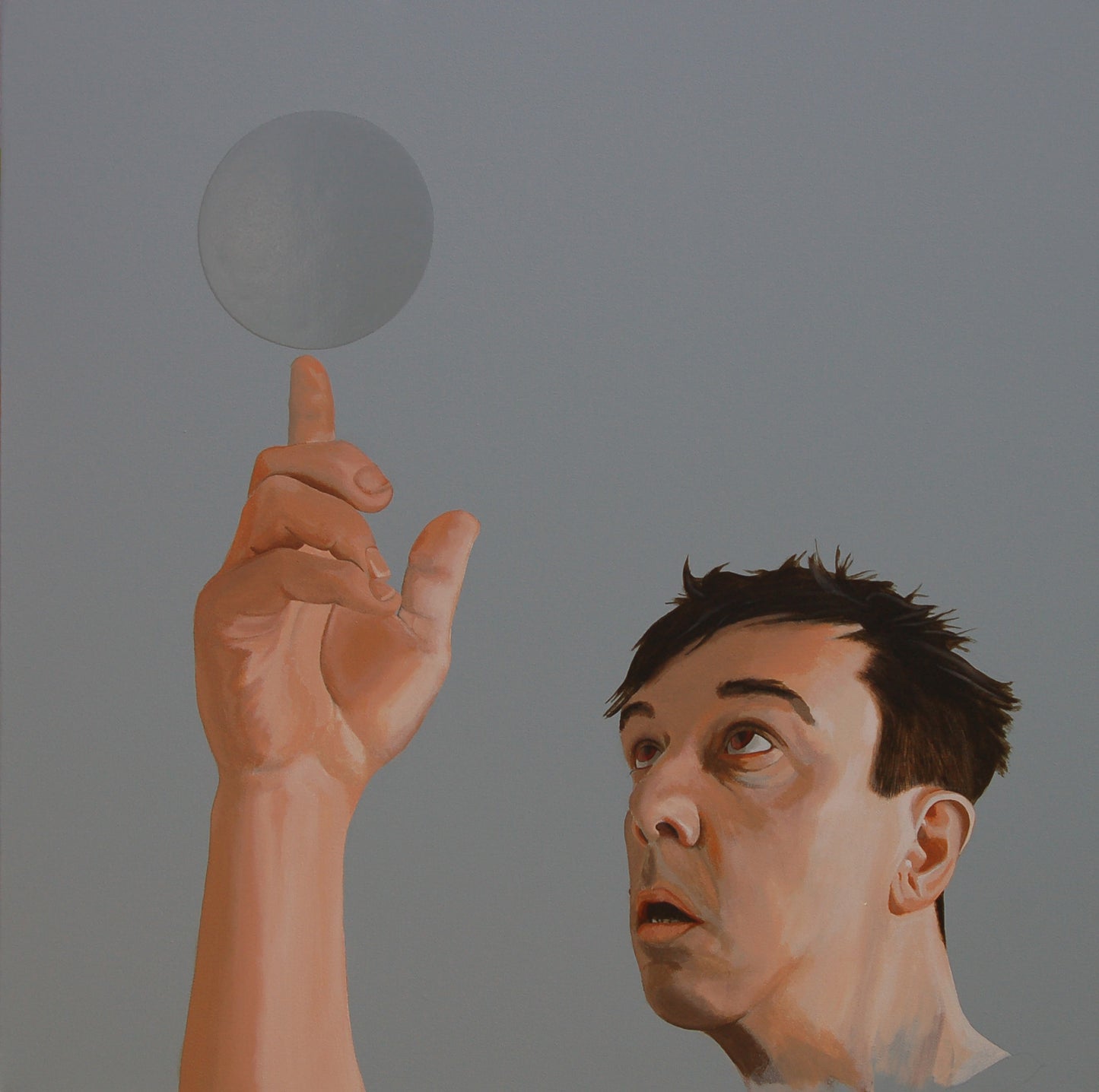 On a light grey background a partially painted self portrait, looking and pointing at a ball of the same colour as the background but in gloss.