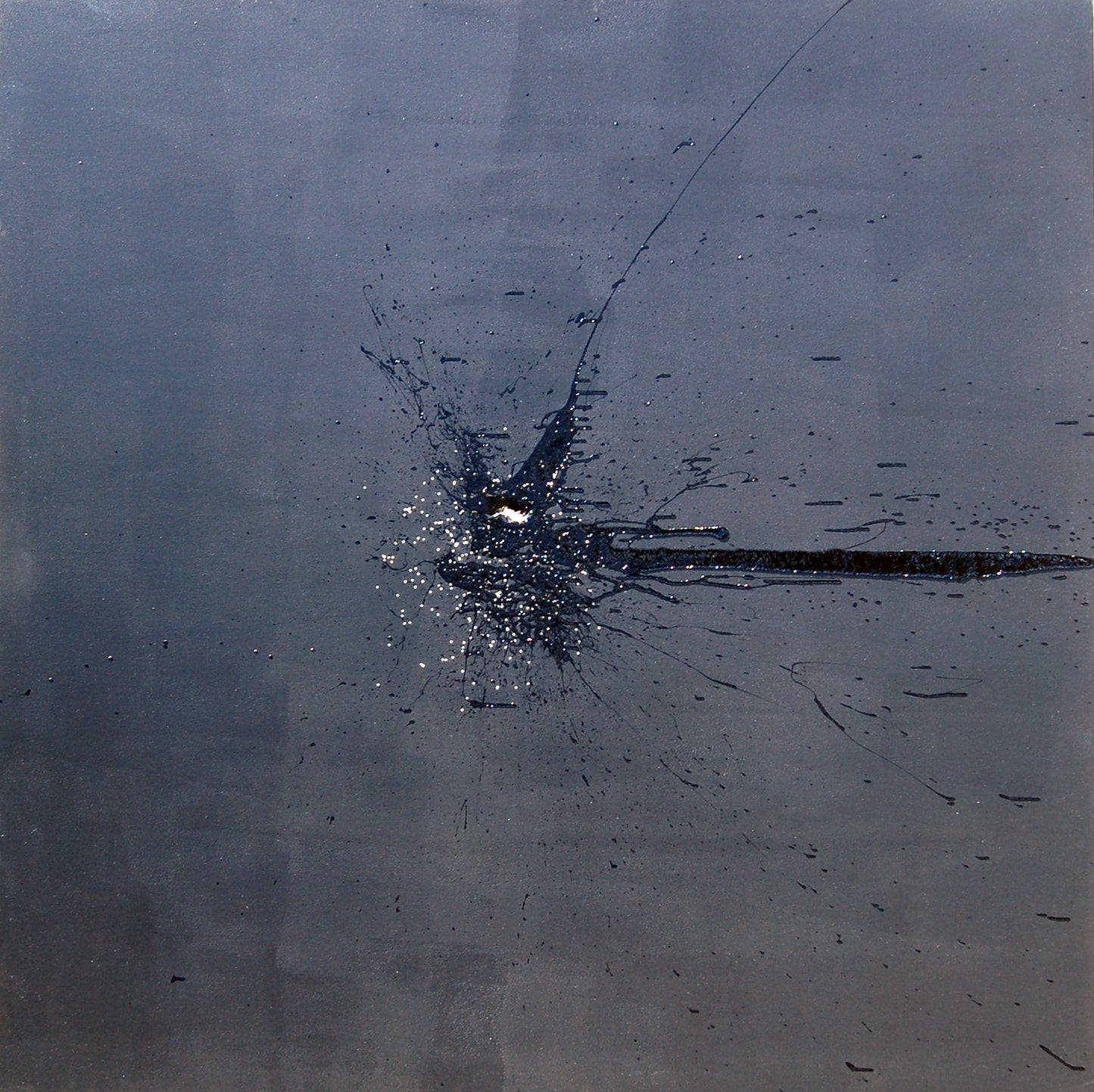 A black mark applied with a shotgun on a dark grey background.